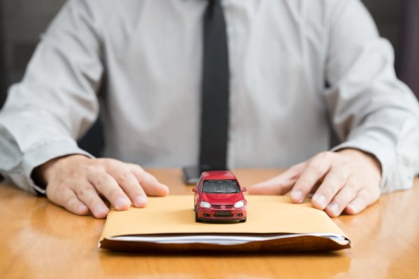 usaa extended vehicle protection service man with black tie on a desk holding paper folder and red toy car above it
